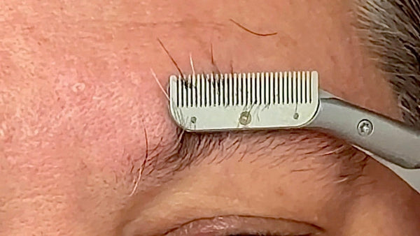 Person using a metal comb on their eyebrow close-up